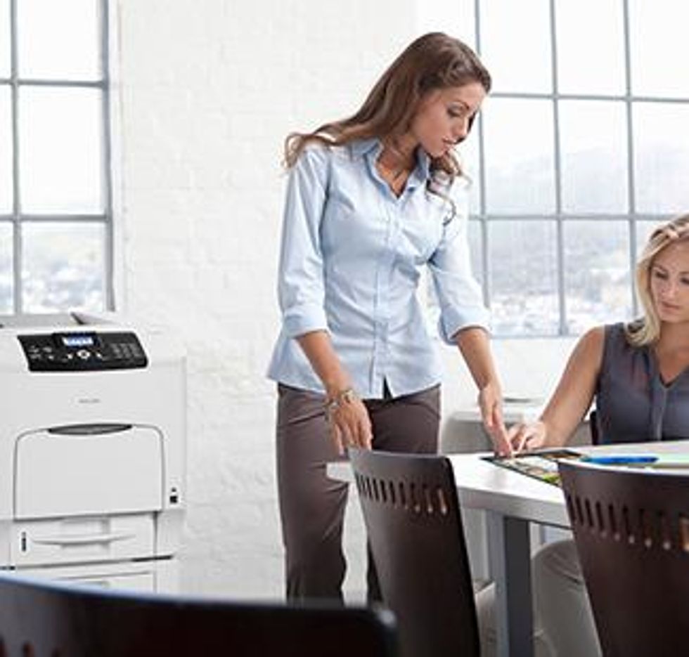 Ricoh Printer in office setting. Two women discussing with paperwork.