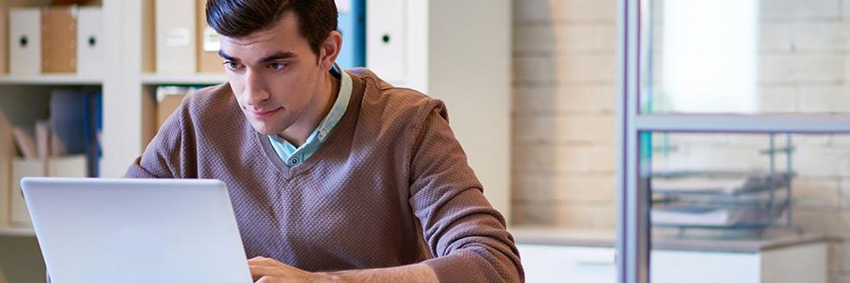 Photo of a man wearing a purple sweater working at his laptop.