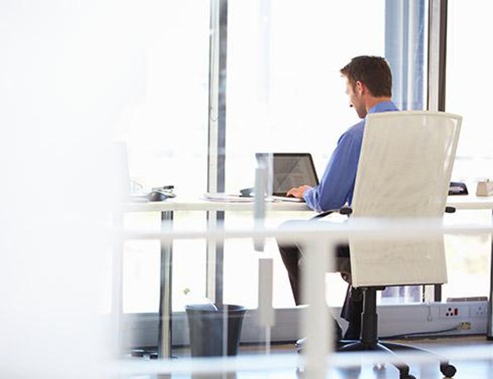 \u200bPhoto of a man in a blue shirt with his back to the viewer, working on his laptop.