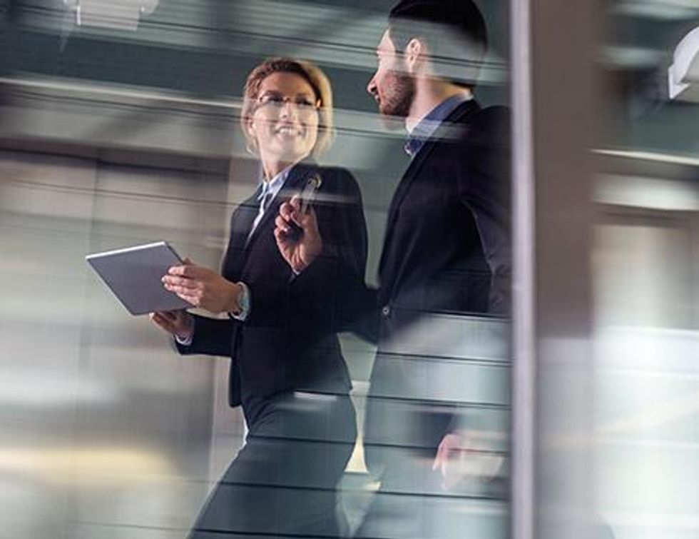 \u200bPhoto of a woman and man walking briskly behind glass.